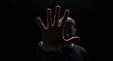 A close up shot of a hand raised towards the camera, fingers slightly spread, blocking the view of a blurred man in the background. photo