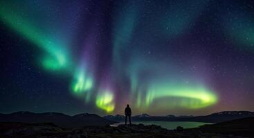 Man gazes at the aurora borealis over the lake and mountain range at night, creating a stunning display of vibrant colors and natural beauty. photo