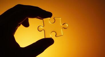 Hand holding a single puzzle piece against a gradient orange background. Illustrates problem solving, decision making, and strategic thinking. photo