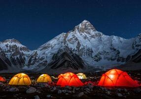 Illuminated tents in a mountain camp under a starry sky. Snowy peaks in the background. Adventure, travel, and outdoor concept with space for text. photo