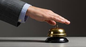 Businessmans hand about to ring a desk bell for service. The concept of customer service, assistance, and attention. Studio shot on gray background. photo