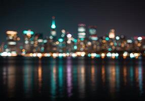 Blurred skyline of San Francisco at night reflecting in the water. City lights create a bokeh effect, with turquoise and orange hues dominating the dark scene. photo
