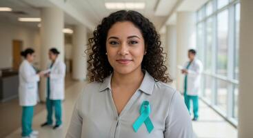 Smiling woman wears teal ribbon for ovarian cancer awareness in hospital hallway with medical staff, symbolizing support and hope for gynecologic cancer patients. photo