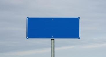 Blank rectangular blue road sign with rounded corners and white border on a gray metal post against a cloudy sky. Space for text. photo