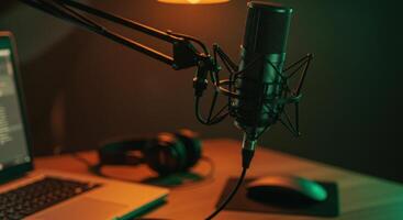 Professional condenser microphone on a boom arm over a desk with a laptop, headphones, and mouse. Studio setup for podcasting, streaming, or voice recording. photo