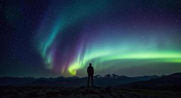Man admires vibrant aurora borealis over mountain range. Night sky filled with colorful swirls of green, blue, and purple lights creates a scenic view. photo