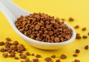 Instant coffee granules in a white spoon on a bright yellow background, showcasing texture and detail. photo