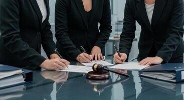 Three businesswomen sign legal documents at a table with a judge gavel. Focus on the agreement signing, representing legal and corporate processes. photo