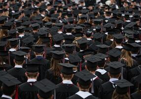 Large crowd of graduates wearing black gowns and mortarboards. Students attending commencement ceremony. Academic achievement and higher education concept. photo