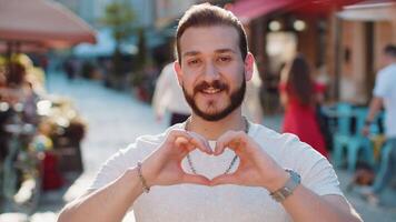 Young man makes symbol of love, showing heart sign to camera, express romantic positive feelings video