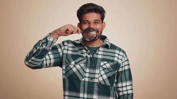 Indian man holding magnifier glass on teeth, looking at camera showing funny smiling face mouth video