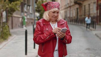 Senior woman use smartphone typing text messages browsing internet finishing work looking at camera video