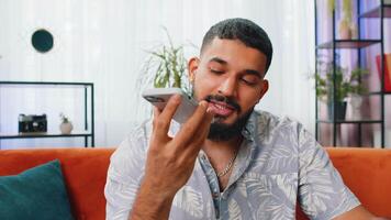 Happy Indian Arabian man making phone conversation with friends sitting call on couch at home room video