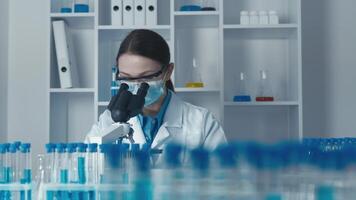 A dedicated female scientist analyzes samples with a microscope, surrounded by colorful test tubes and essential lab equipment, highlighting the significance of research and innovation in her field video