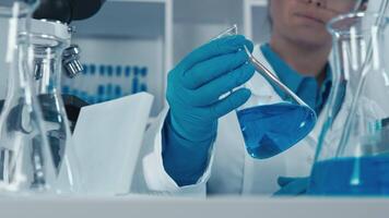 A dedicated scientist in a white lab coat carefully examines blue solutions using laboratory glassware, showcasing the intricate processes of scientific research and experimentation. video