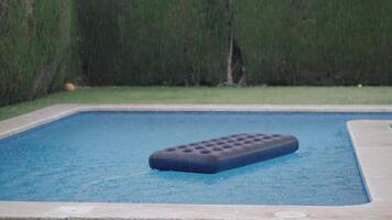 Inflatable mattress floating in backyard pool during light rain video