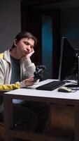 vertical Bored gamer sitting at desk holding controller looking at computer video