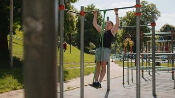 Athletic man in sportswear doing pull-ups exercises on horizontal bar with help of elastic expander video