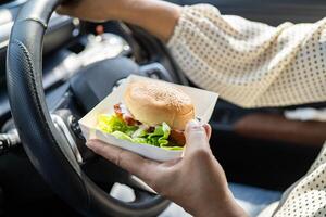 Asian woman driver hold and eat hamburger in car. photo