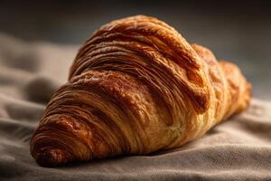 Golden, flaky croissant with crisp, layered texture rests elegantly on soft, rustic fabric, showcasing intricate pastry details and rich, warm tones under gentle, natural lighting photo