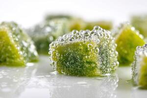 Green cube with surface covered in small bubbles, surrounded by more blurred green cubes. The light, reflective surface beneath hints at moisture or condensation, enhancing depth photo