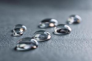 Transparent water droplets scattered on a smooth, textured gray surface, each droplet reflecting light, creating an artistic and fresh atmospheric scene photo