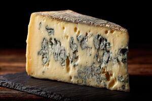 A wedge of blue cheese with a crumbly texture lies on a rough slate surface, displaying its distinctive blue veins and creamy color under a soft, focused light photo