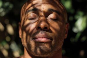 Serene expression of a person with closed eyes, sunlight filtering through leaves casting striped shadows on their face. The play of light and shadow creates a calming atmosphere photo
