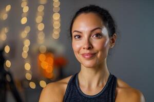 Smiling woman with dark hair in a sleeveless top, blurred warm-toned bokeh lights in the background, creating a soft and inviting atmosphere photo