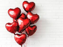 Red heart-shaped balloons clustered together against a white brick wall, creating a vibrant and cheerful display. Reflections highlight the glossy surface of the balloons photo