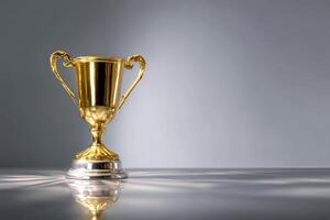 Golden trophy with elegant handles on a reflective surface, casting subtle shadows. The lighting emphasizes the shiny metallic texture and polished silver base, creating a sense of achievement photo