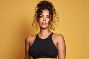 Curly-haired woman wearing a black sleeveless top gazes confidently with a calm expression. Hair is styled in an updo with loose curls framing the face. Lighting highlights skin tone photo
