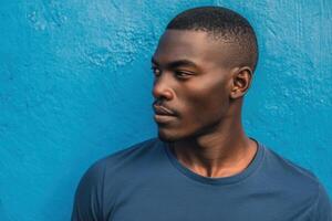 Young man with short haircut wearing a dark blue t-shirt, facing right, set against a vivid blue textured wall, exuding a calm and thoughtful expression, in profile view photo