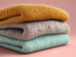 Three knitted sweaters in mustard yellow, light gray, and mint green are stacked neatly. The textured fabric creates a cozy, warm impression, highlighting the knit patterns photo