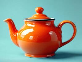 Bright orange teapot with a glossy finish, featuring a round body, a matching lid with a knob, curved spout, and elegant handle, set against a smooth turquoise backdrop photo