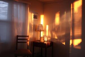 Warm sunlight casts glowing orange reflections on the wall of a cozy room. A wooden chair and small table with a lamp and two glasses create a serene, inviting atmosphere photo