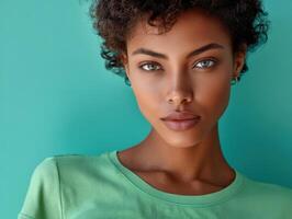 Curly-haired individual with striking eyes and wearing a green top looks directly at the camera, exuding confidence and poise. The vivid color contrasts beautifully with the subject's features photo