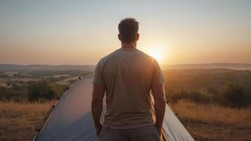 Man standing in front of tent at sunset photo