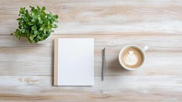 A blank notebook, a cup of coffee and a plant on a wooden table photo