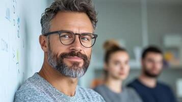 A man with glasses and a beard standing in front of a white board photo