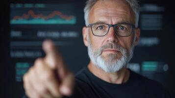 A man with glasses and a beard pointing at a screen photo