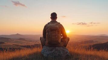 Man sitting on rock at sunset with backpack photo