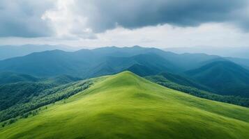 A green hill with trees and mountains in the background photo