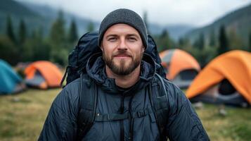 A man with a beard and backpack in front of tents photo