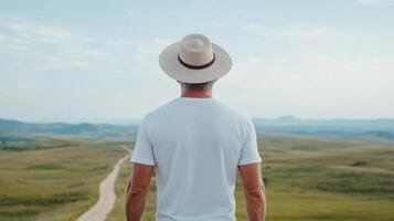Man in hat standing on road looking at countryside photo