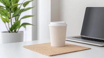 A coffee cup on a table with a laptop and a plant photo