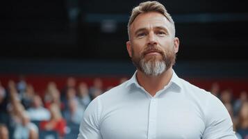 A man with a beard and white shirt standing in front of an audience photo