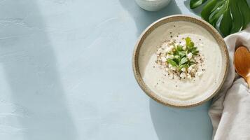 A bowl of creamy soup with a spoon and a leaf on a blue background photo