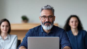 A man with glasses and beard sitting in front of a laptop photo