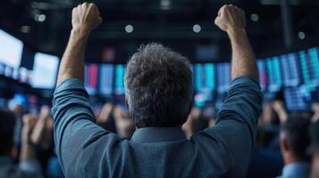 Man raising his hands in front of a stock market screen photo